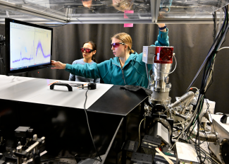 JILA graduate students Na Li (left) and Anya Grafov (right) look at a laser array system.