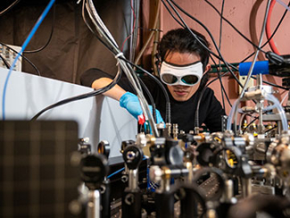 JILA graduate student Qizhong Liang bends over a frequency comb set up in the JILA laboratory.