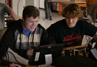 two students sitting next to each other looking at a tablet screen and smiling 
