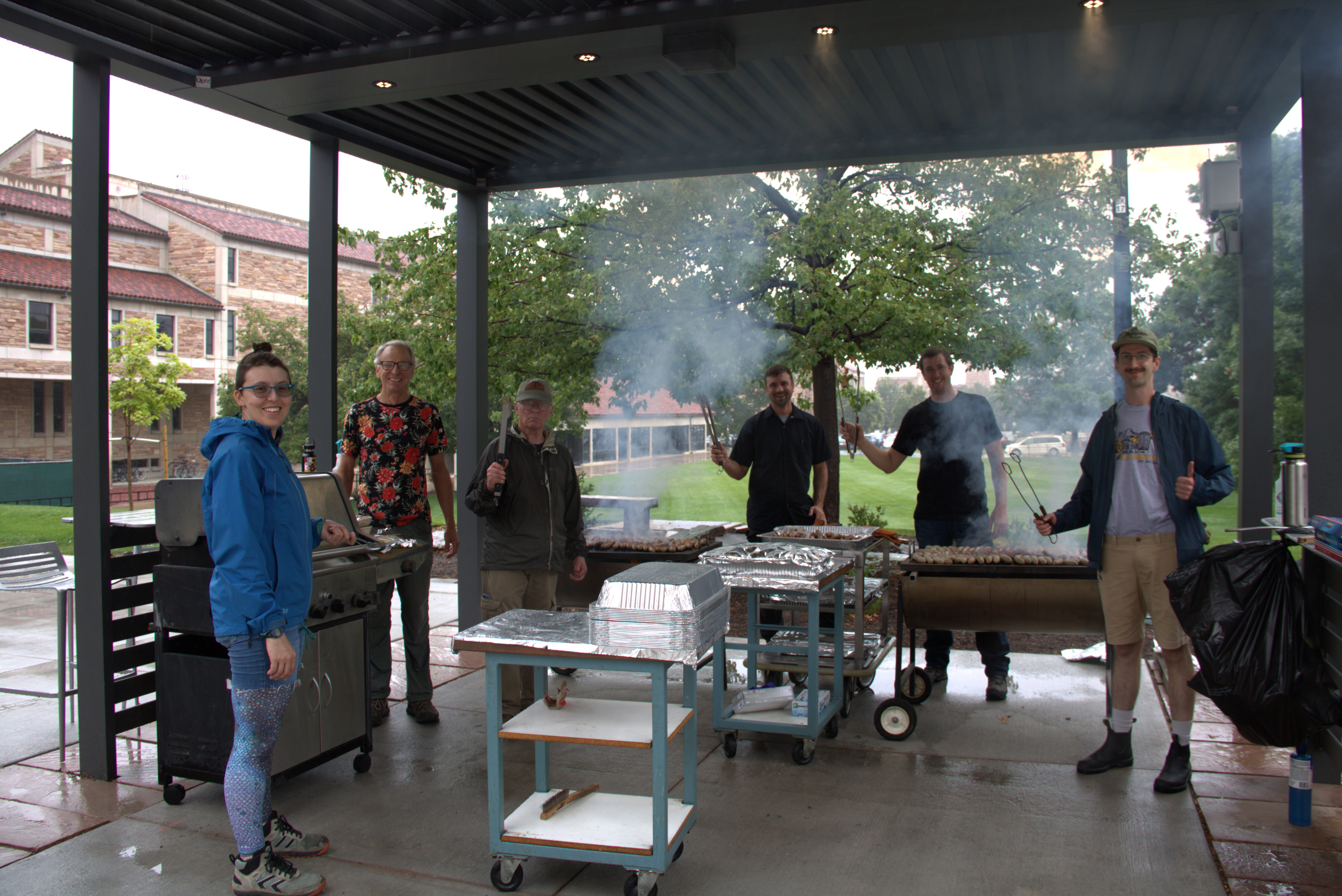 Members of the instrument shop smile while cooking over 500 brats for the annual JILA brat cookout